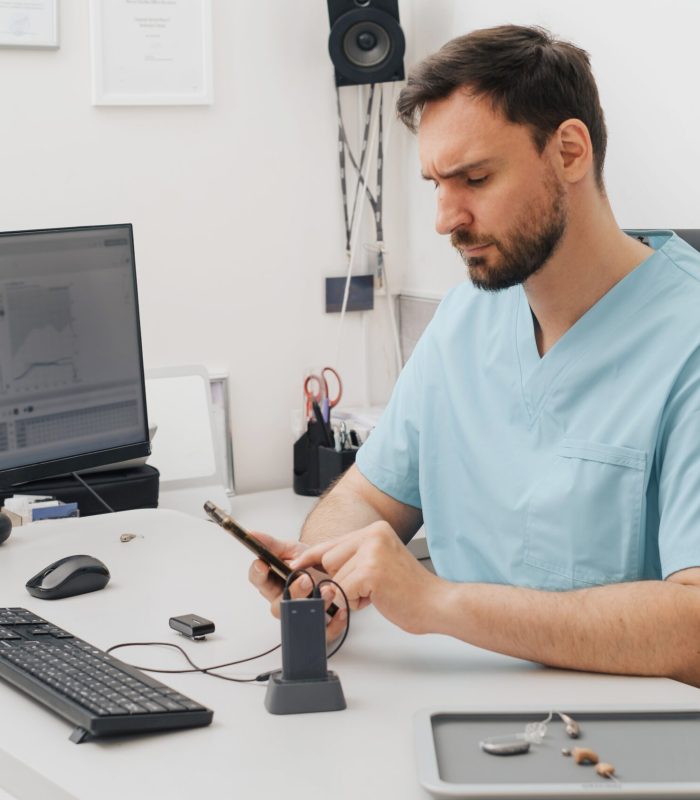 Otolaryngologist at modern medical center. Portrait of audiologist who assess disorders of hearing working with smartphone and computer. Copy space